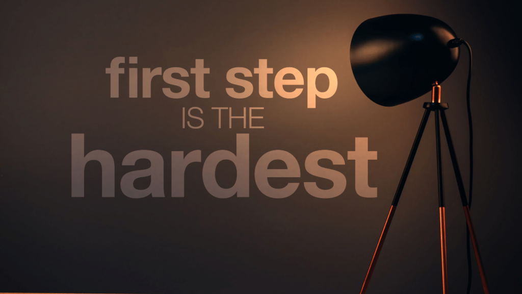 Black lamp shining light on the words "first step is the hardest" written on the wall